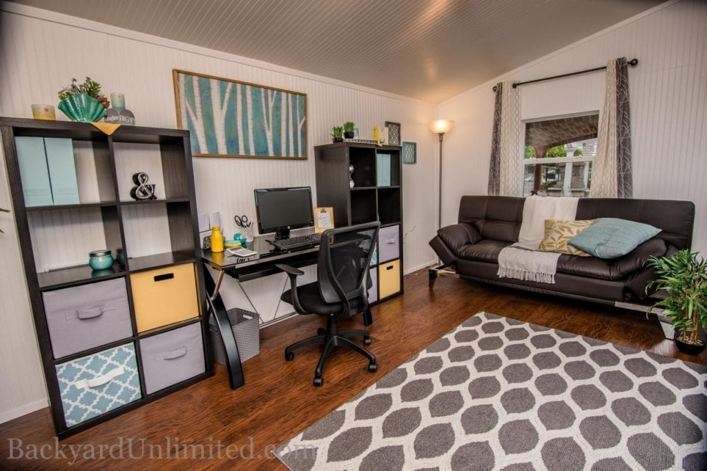 Studio shed interior with computer desk, shelving and a brown leather couch.